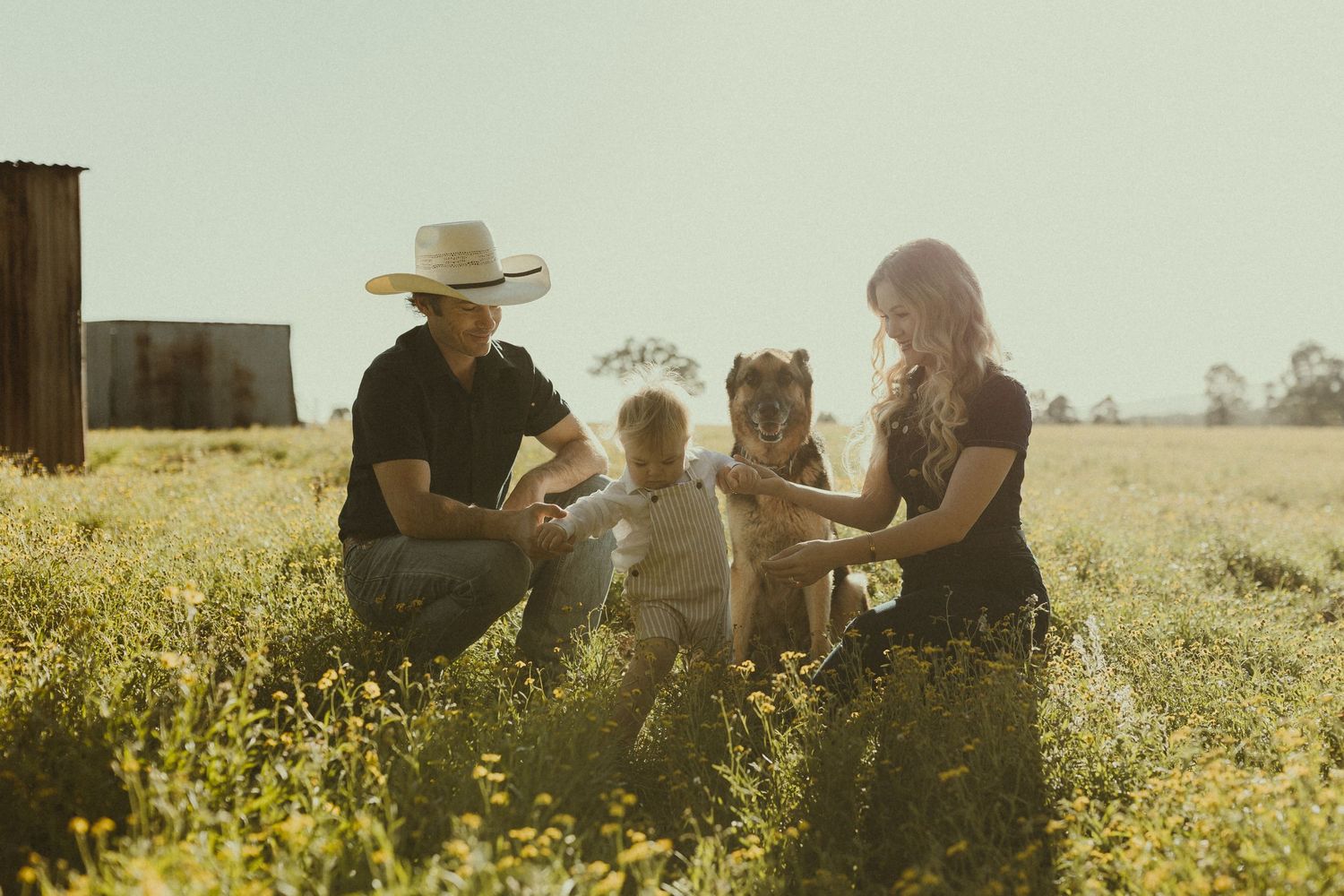 People gather in a sun-drenched field of yellow wildflowers during golden hour creating a warm pastoral scene.
