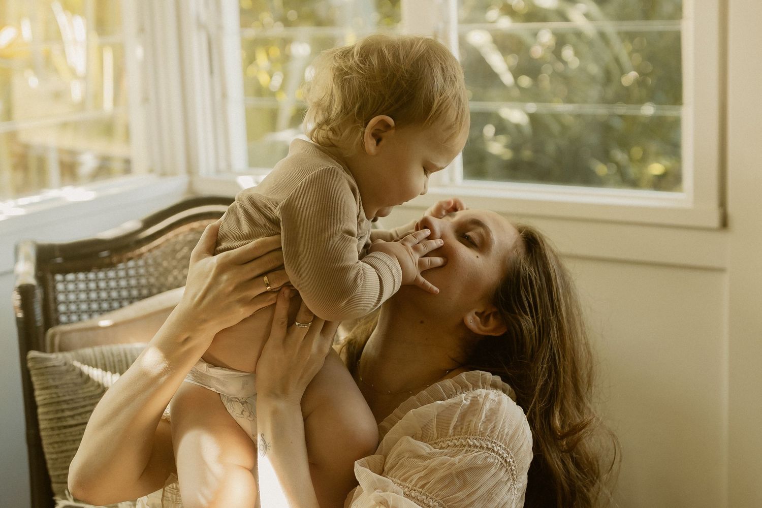 Four sequential photos show a tender moment between a parent and baby in a sunlit room.