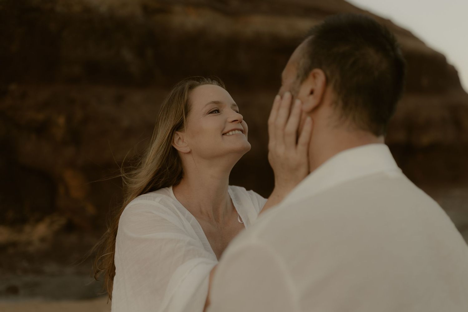 Intimate romantic moment captured against textured rock formations at sunset.