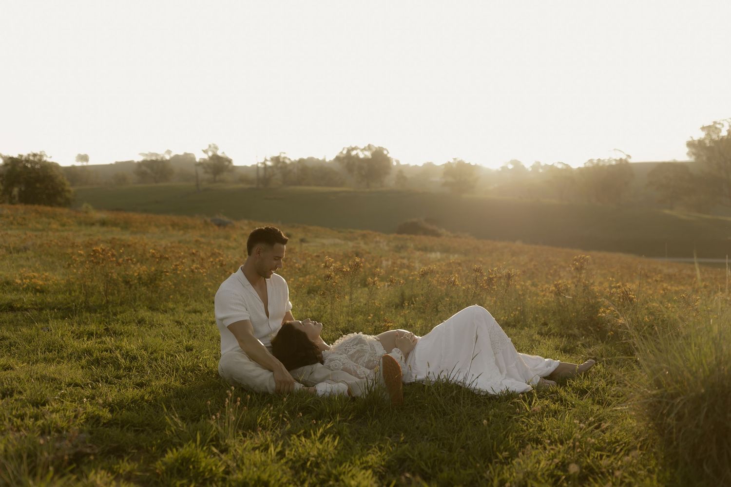 Couple shares tender moments while sitting in a golden meadow during sunset.