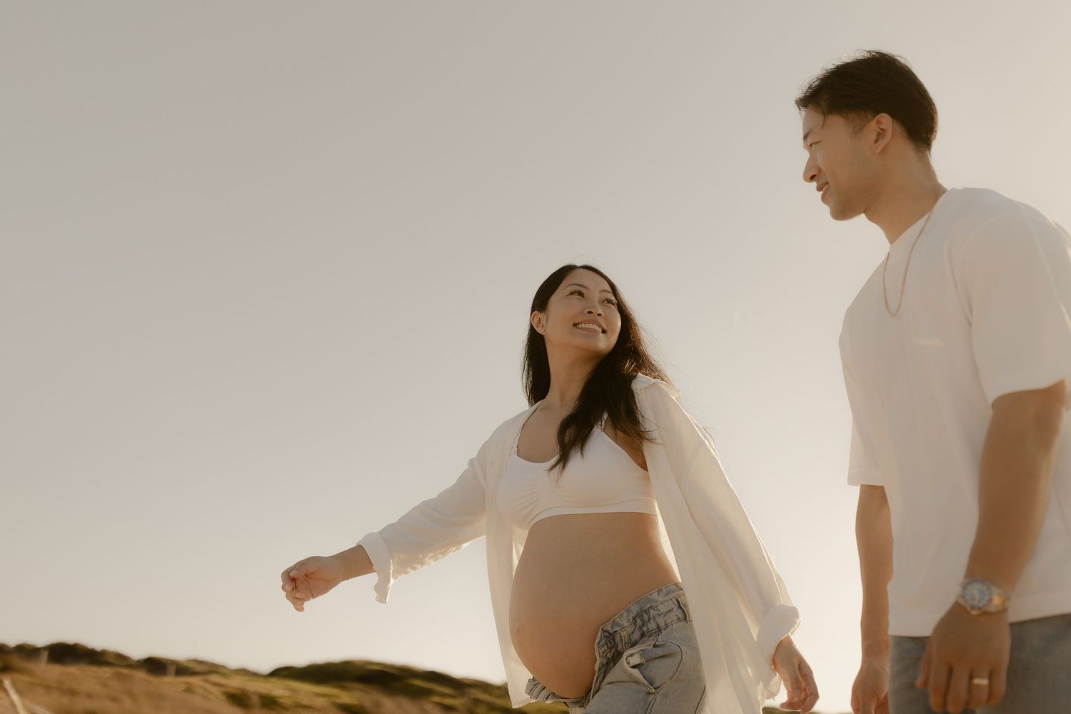 Couple in white outfits sharing tender moments against minimalist white background.