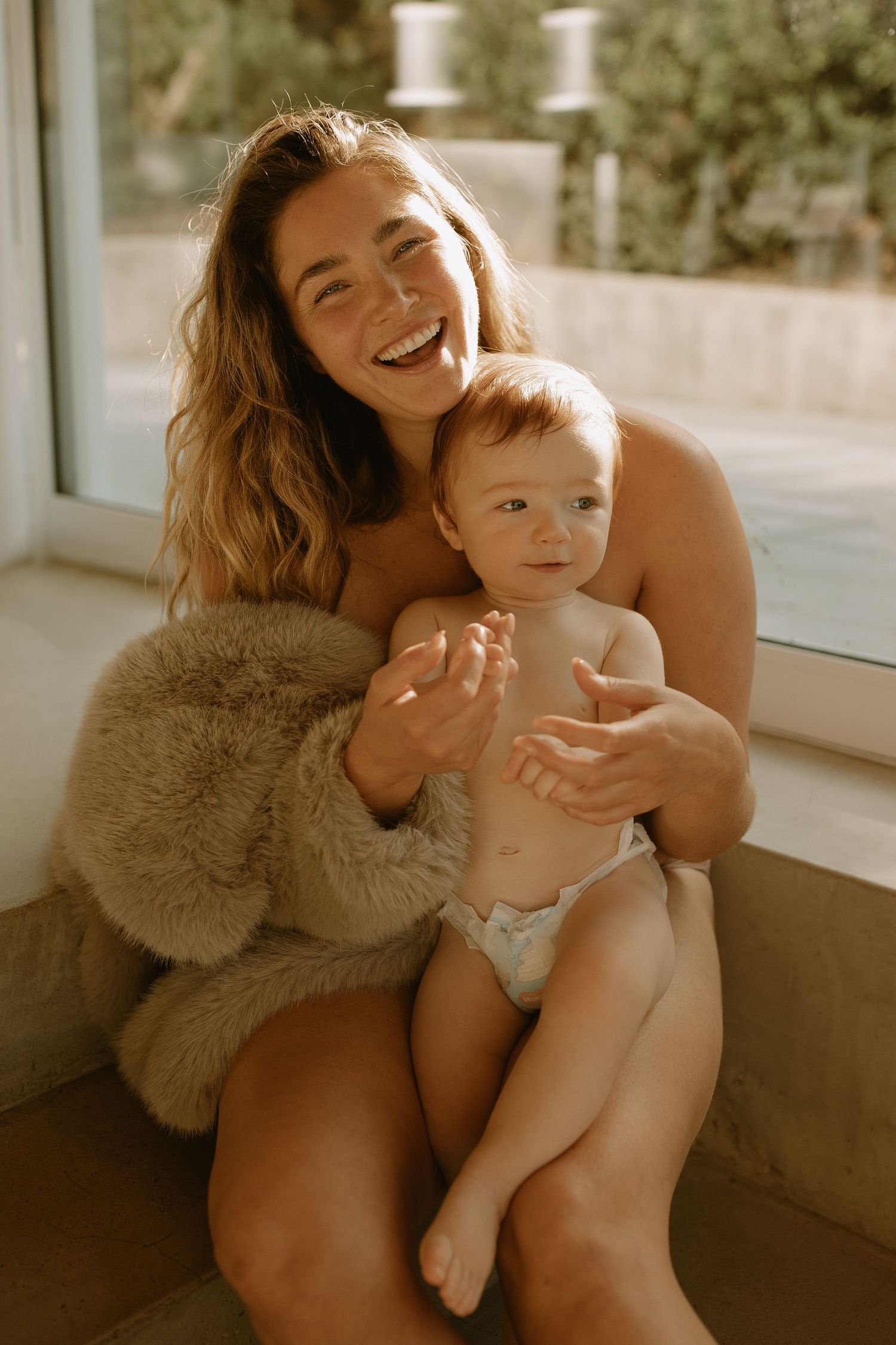 A candid moment of laughter and bonding between parent and baby sitting by a sunny window.