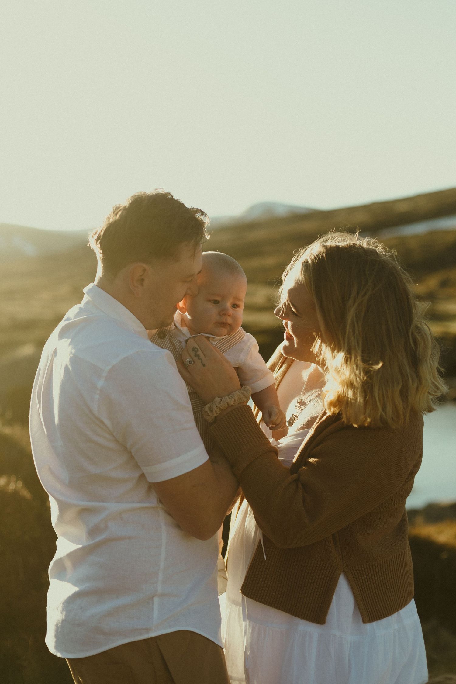 Family in white and brown outfits share an intimate moment together during golden hour in a beautiful outdoor setting.