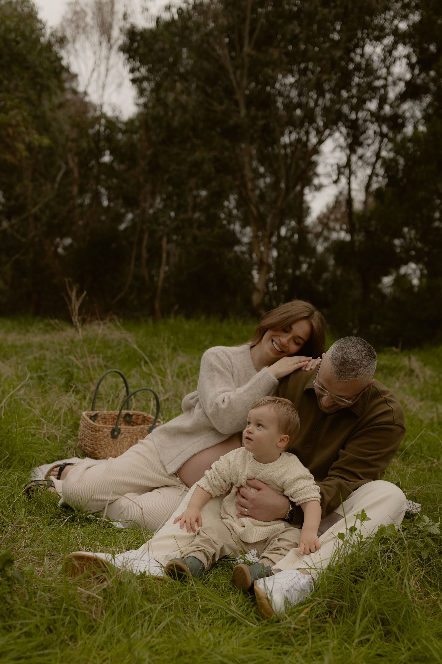 Family sitting on grass in a lush green park, parents lovingly holding their baby during a peaceful outdoor picnic.