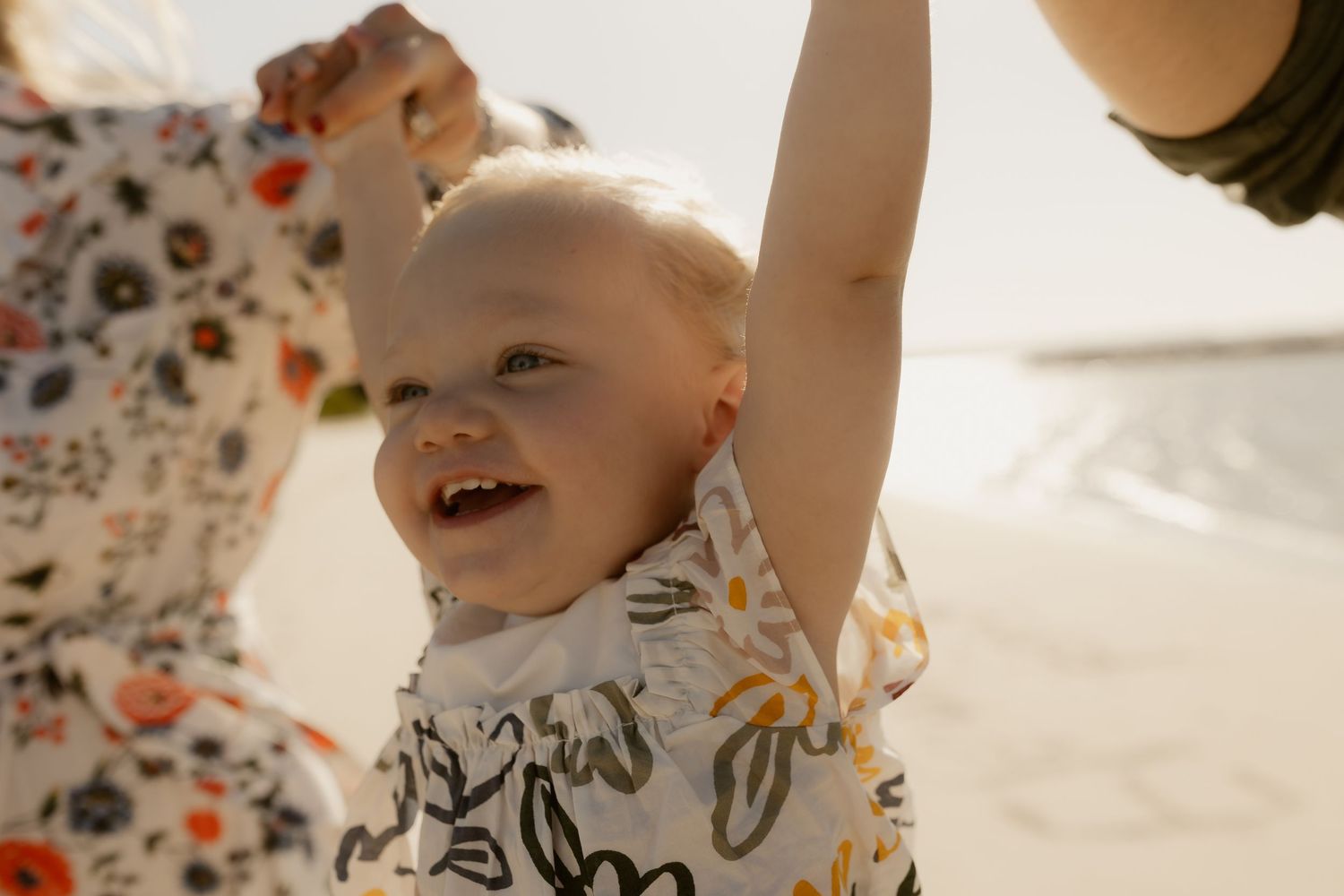 Child reaching up joyfully while playing outdoors in floral printed clothing.