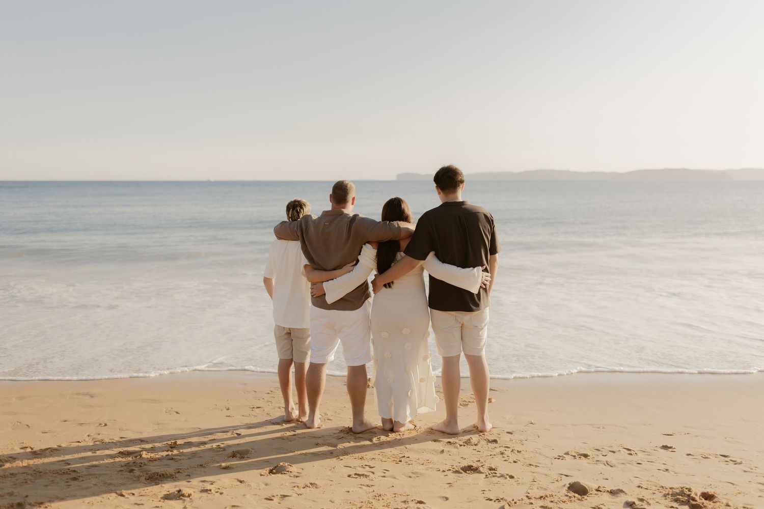 Group sitting together on sandy beach watching the ocean waves at sunset.