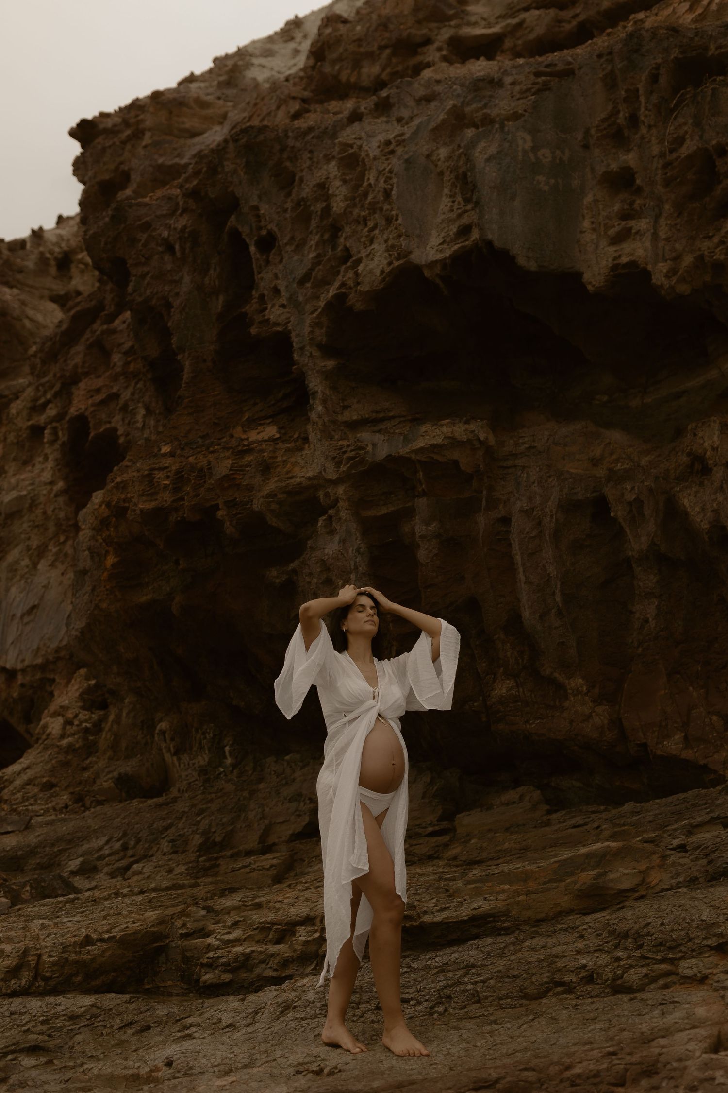 Two people in white outfits pose playfully against rocky coastal cliffs in vintage-style sepia photography.