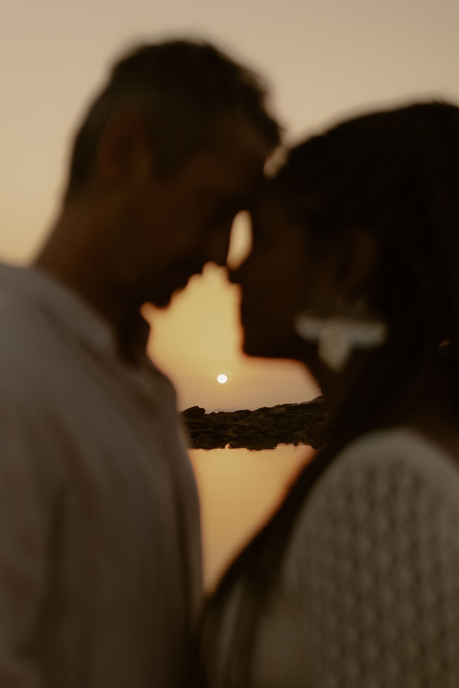 A silhouetted couple shares an intimate moment against a warm sunset backdrop in a romantic outdoor setting.