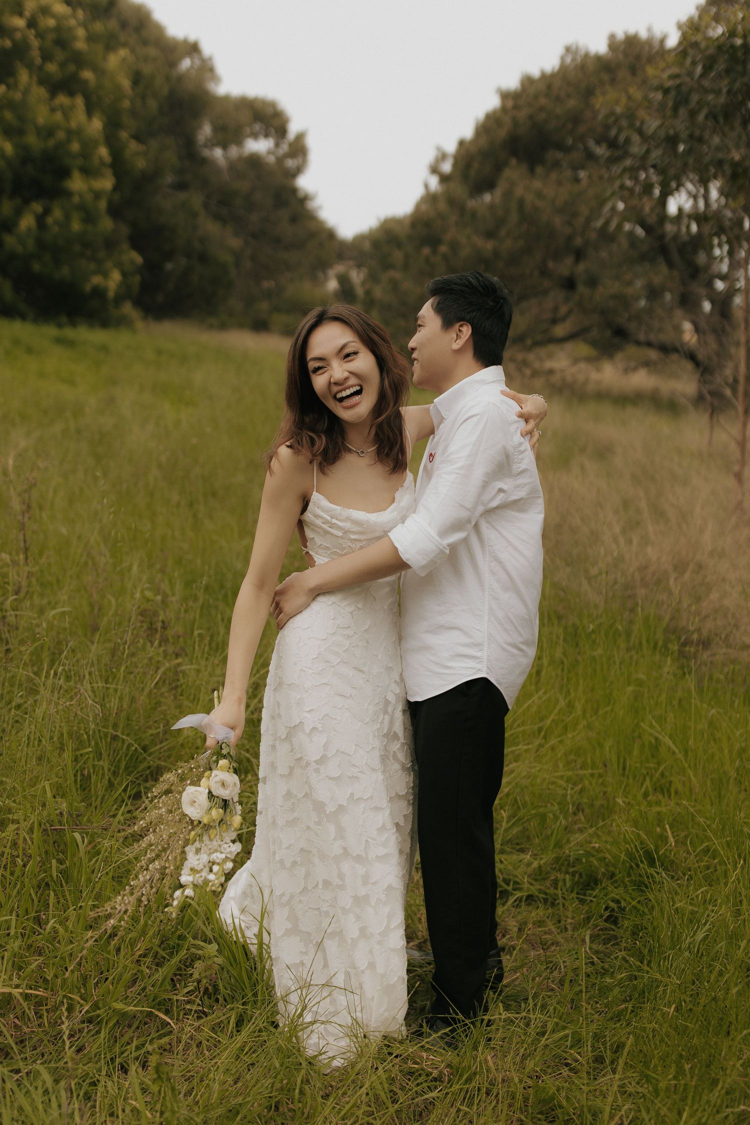 A couple embraces while standing in tall grass during their wedding photoshoot.