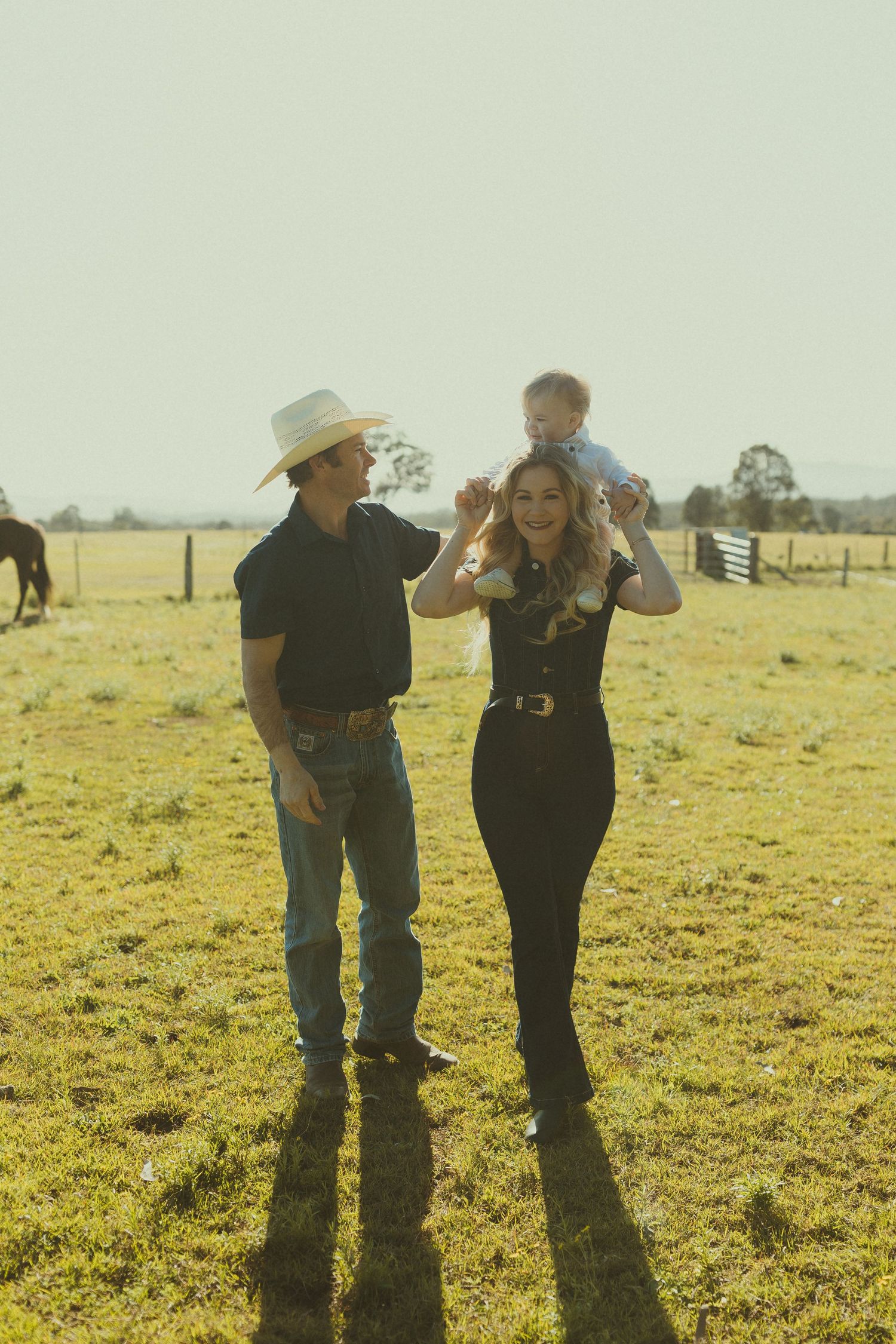 Family walking together across a sunny pasture in casual western wear.