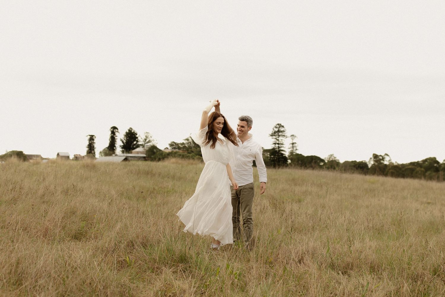 A couple walks hand in hand through a serene golden field during sunset, creating a romantic silhouette.