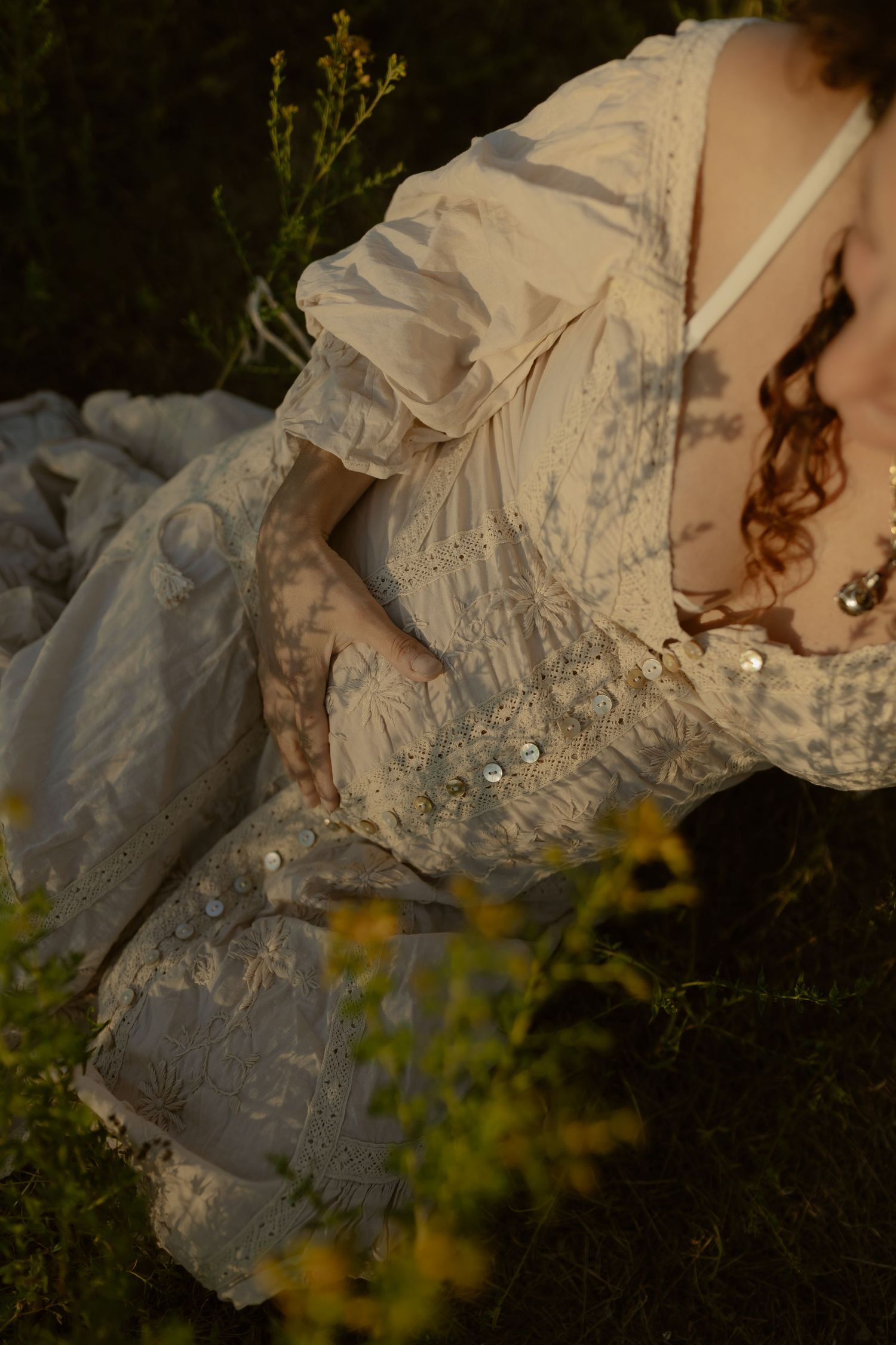 Detail shot of delicate white lace dress fabric against yellow wildflowers.