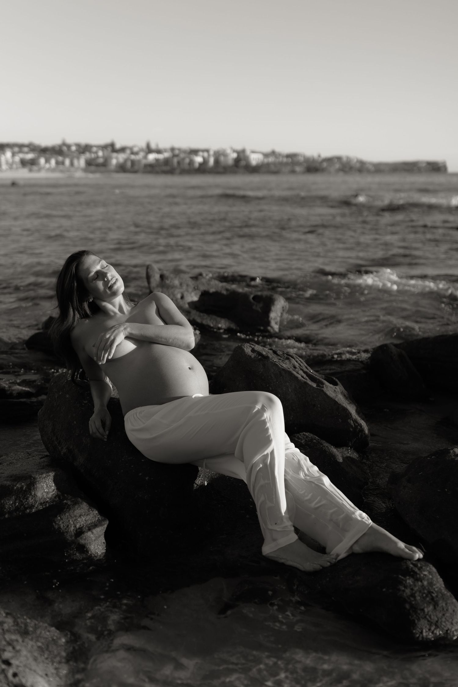 Black and white photo series of a person lounging on coastal rocks by the ocean.