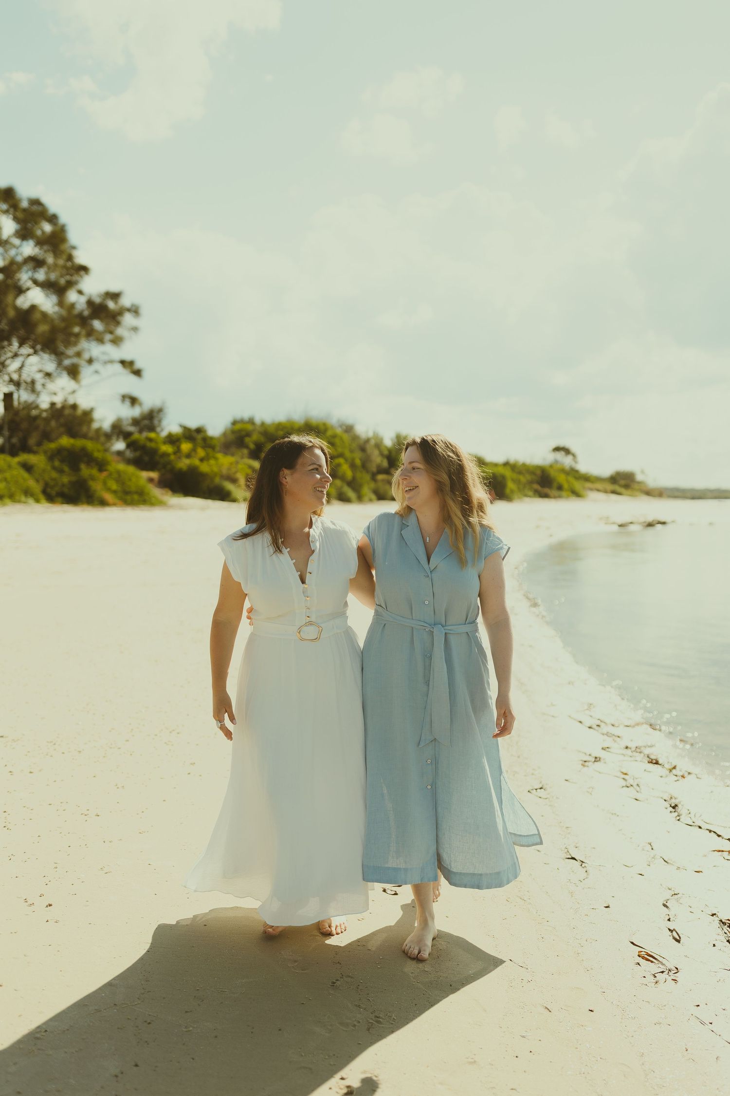 Two people in light colored clothing stroll together on a pristine white sandy beach.