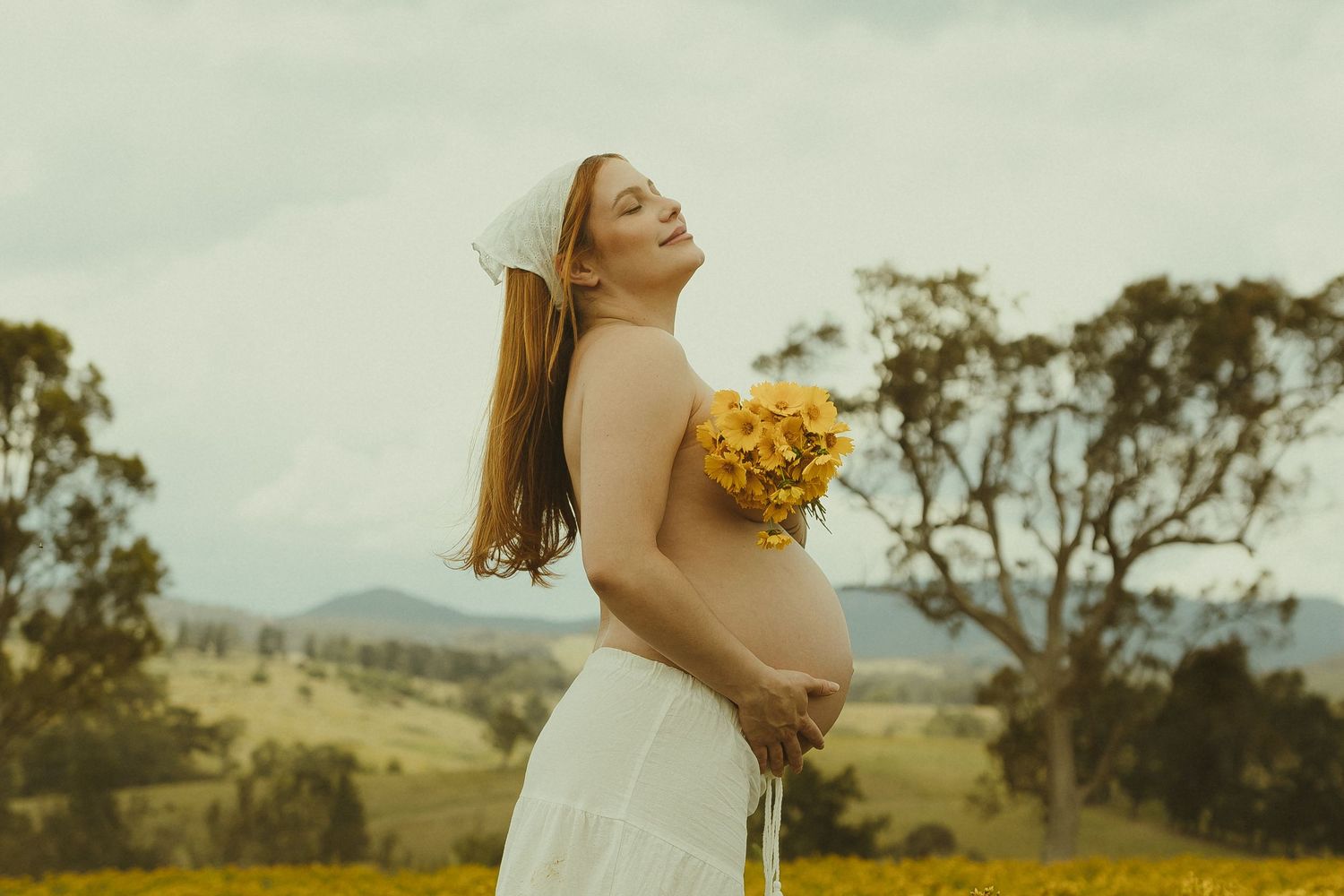 A romantic moment captured in a golden meadow with rolling hills and scattered trees in the background.