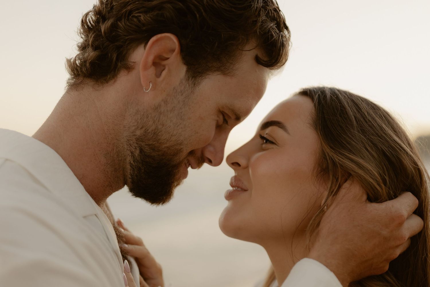 A romantic couple shares an intimate moment at sunset in a natural outdoor setting.