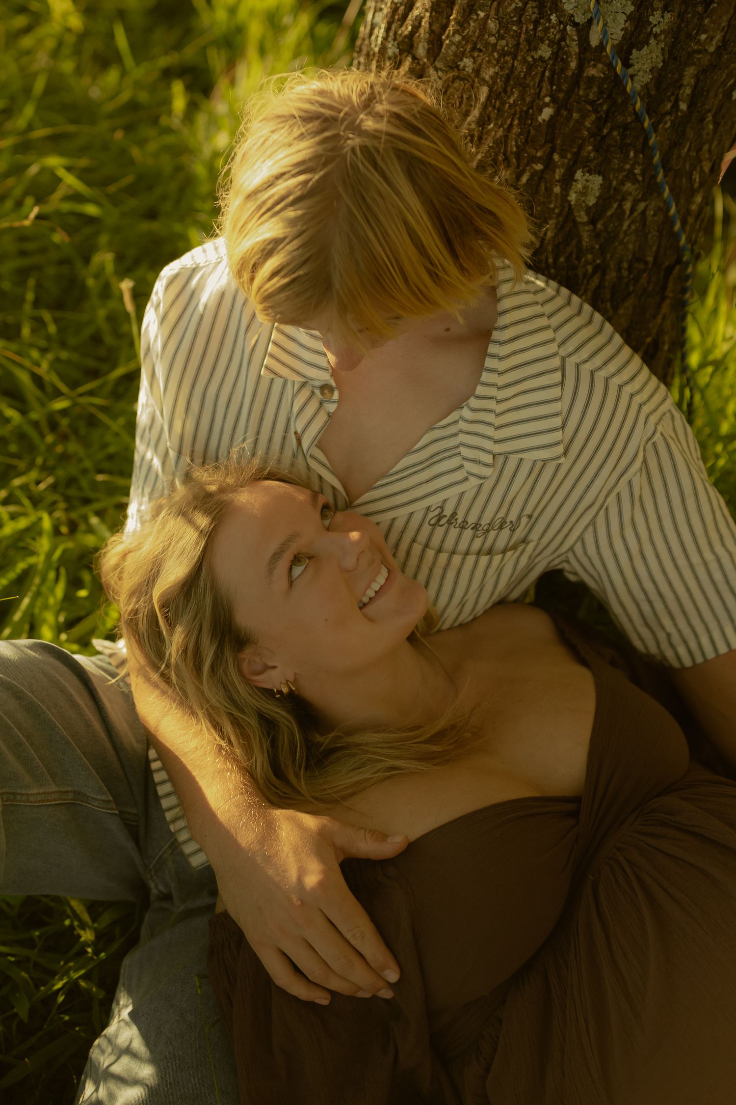 Sun-drenched portrait of two people sharing a tender moment against a tree.
