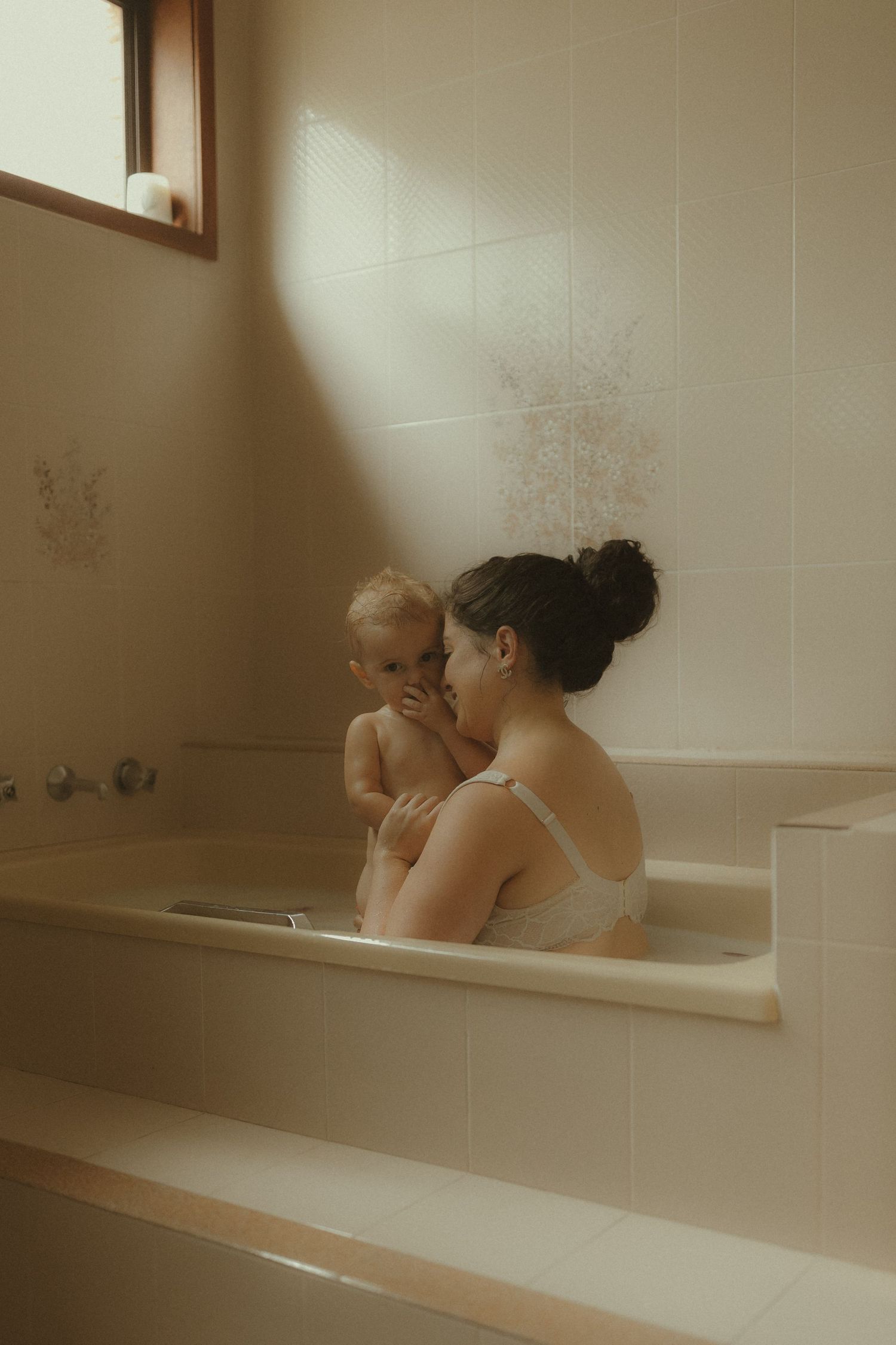 Parent and baby sharing a peaceful moment together in a sunlit bathroom.