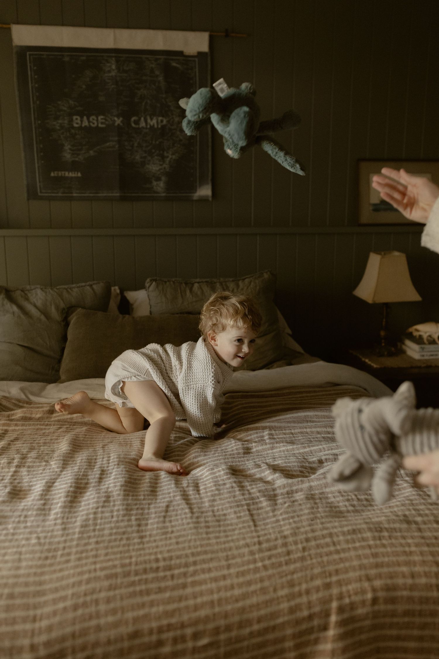 Cozy bedroom scene with a small child playing on striped bedding near a chalkboard wall.