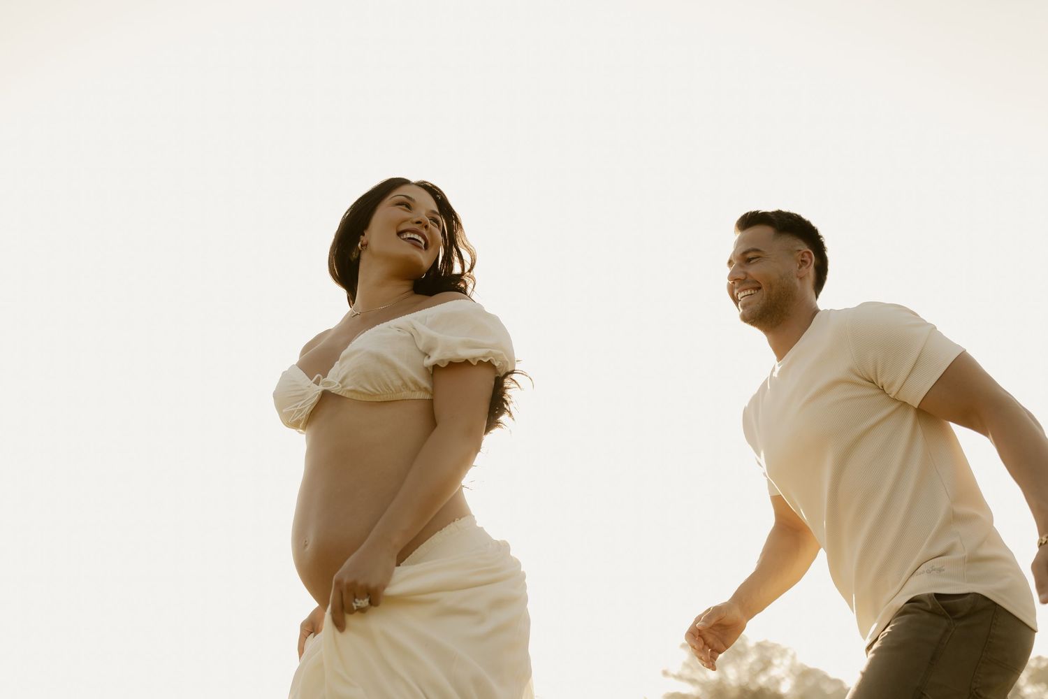 Joyful couple laughing and dancing together in a sunlit outdoor setting.