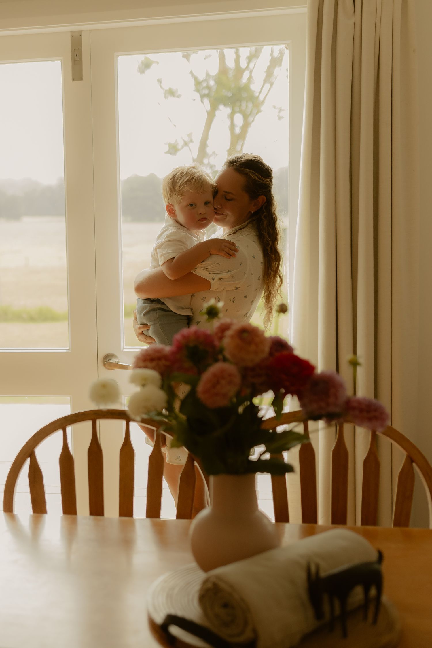 A dining room scene with flowers in vase by bright windows.