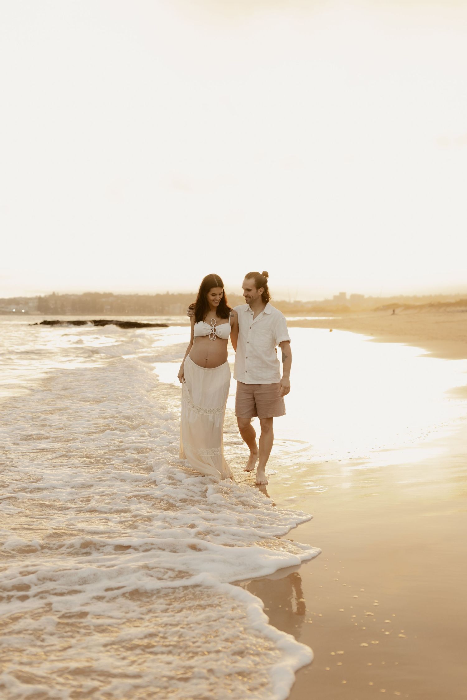 A couple walks along the beach shoreline during golden hour.