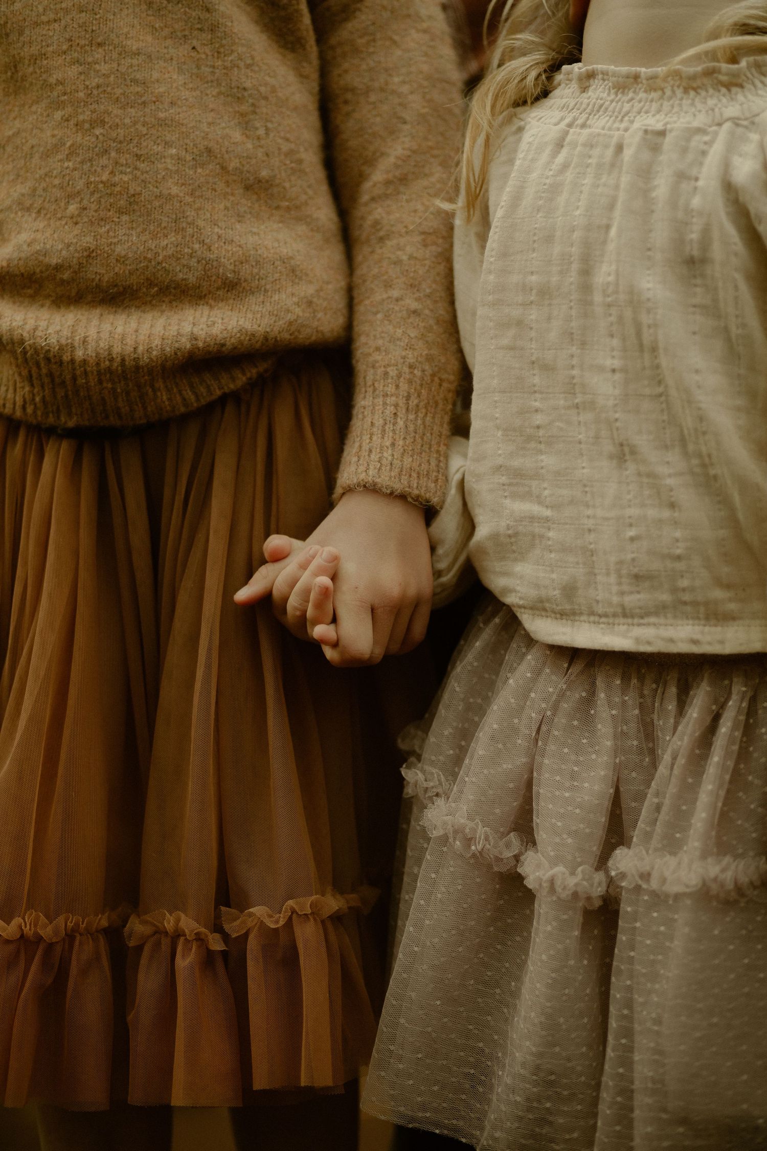 Two people in vintage-style dresses holding hands, wearing brown and cream colored ruffled skirts and sweaters.