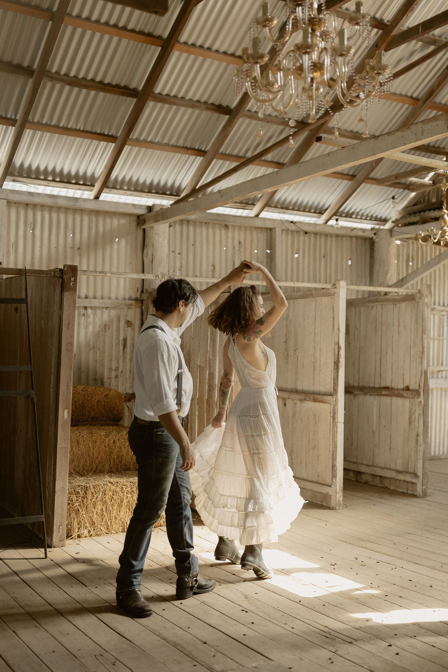 Two people dance together in a rustic barn interior with wooden floors and corrugated metal walls.