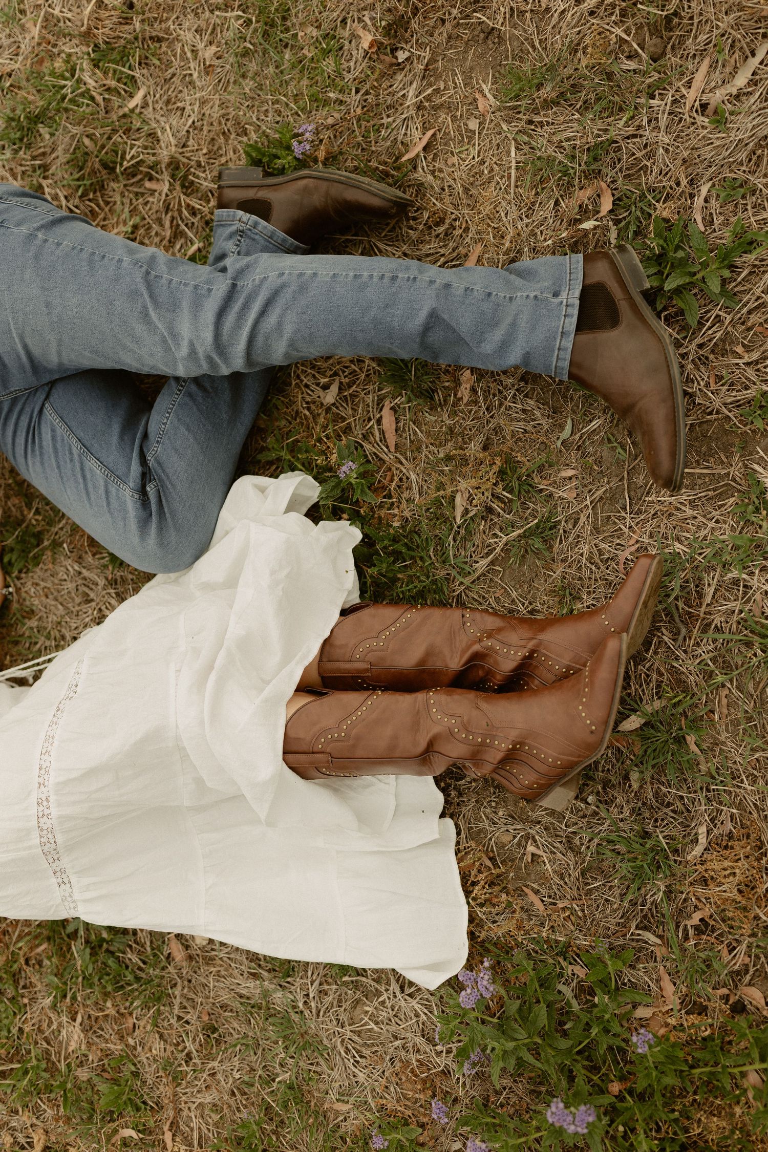 A pair of brown boots and gray clothing lay scattered on dried grass and earth.
