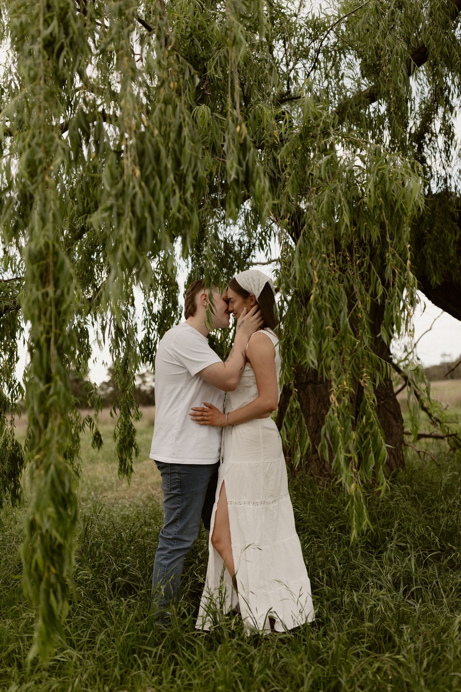 Couple sharing an intimate moment under drooping willow tree branches.