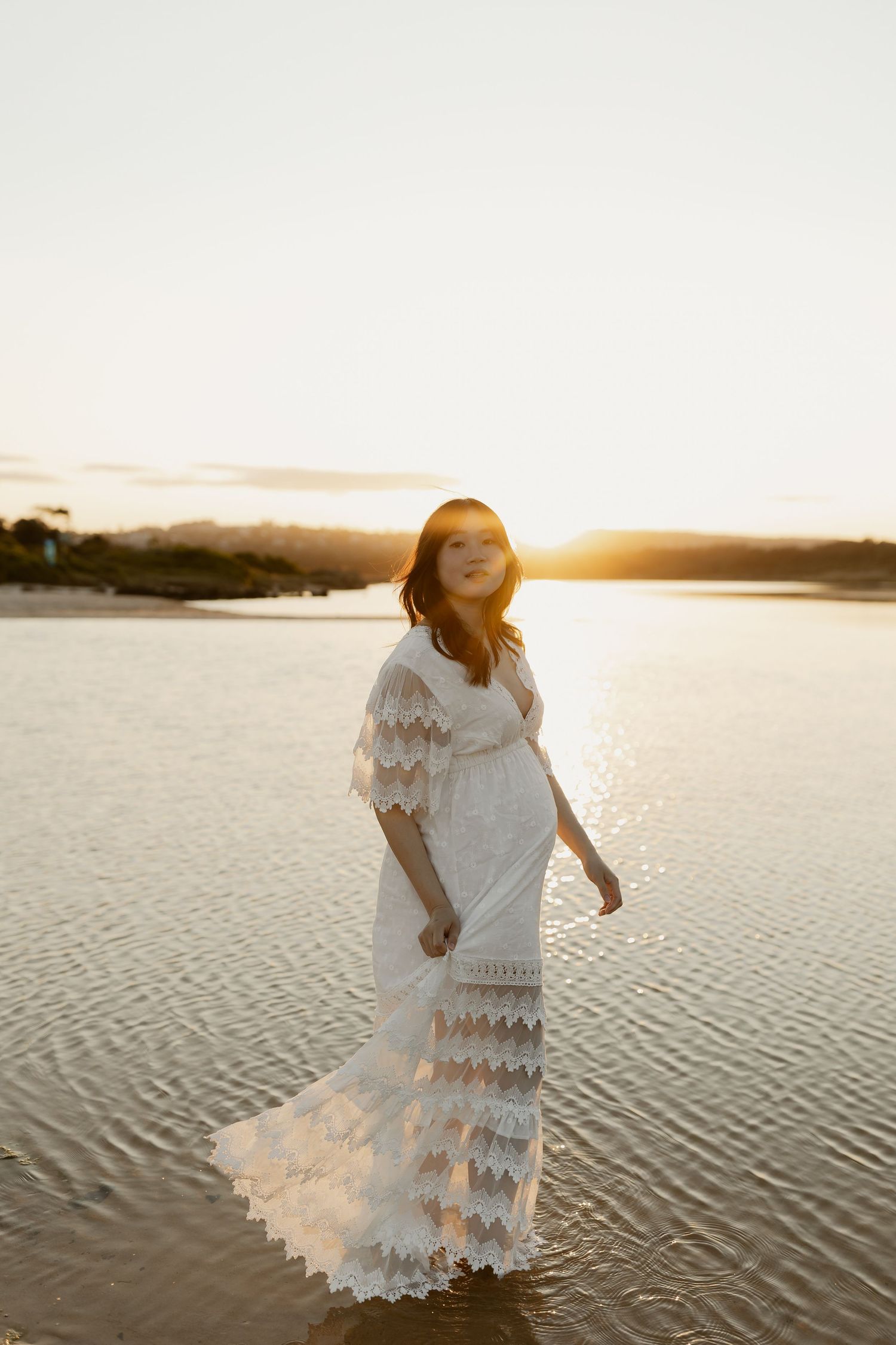 A person in a flowing white lace dress twirls on a beach at sunset, creating an ethereal silhouette against the golden light.