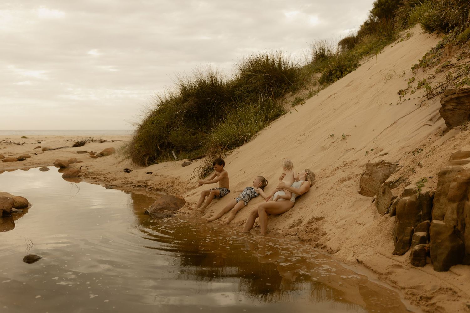 People relaxing on sandy rocks by the water's edge during a peaceful beach day.