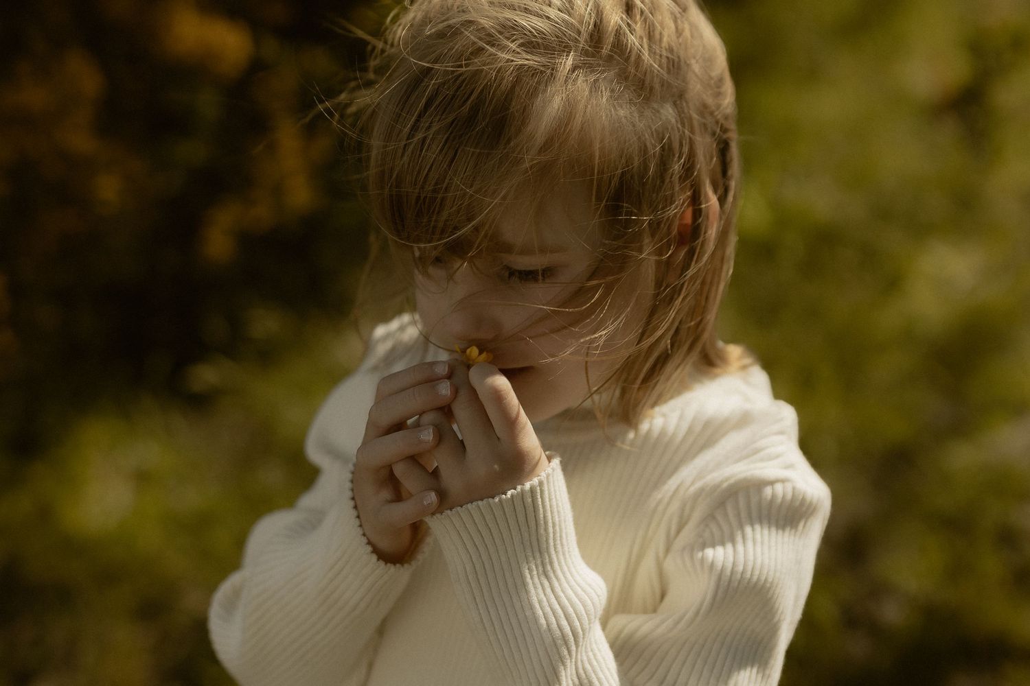A person wearing a cream colored sweater is photographed in a natural outdoor setting with warm autumn lighting.