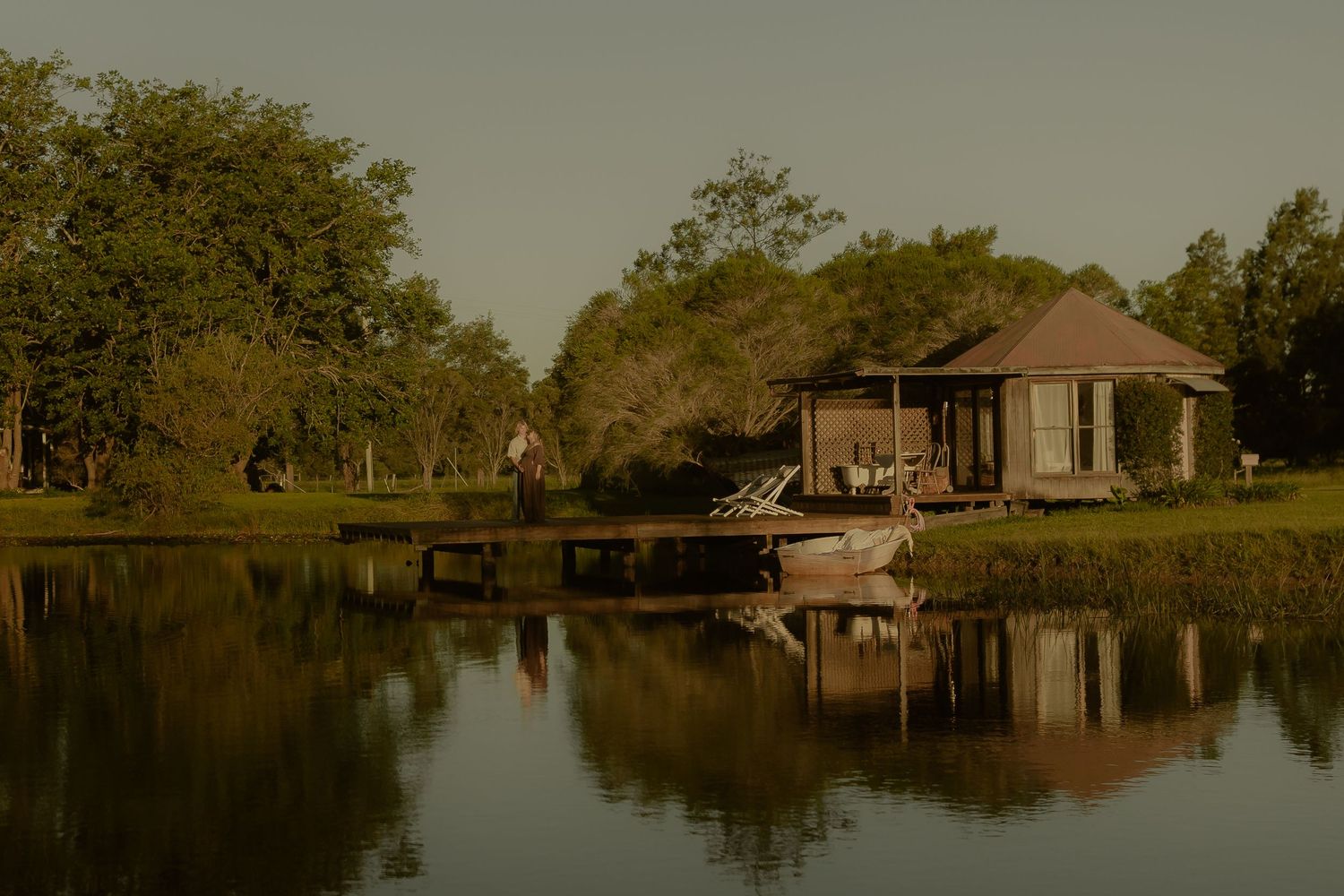 Rustic lakeside gazebo with wooden dock reflects perfectly in still waters during golden hour.