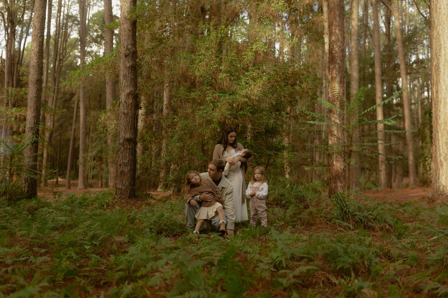 Mother in white dress with two young children standing in a lush green forest.