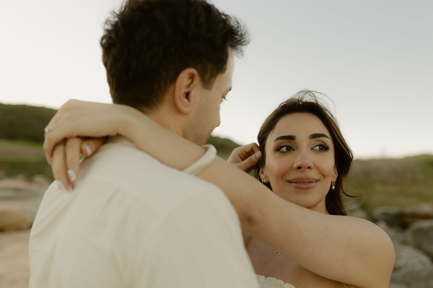 A bride gazes lovingly at her groom outdoors during golden hour, her arms wrapped around his neck at their wedding.