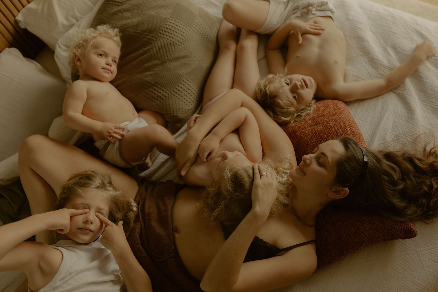 A family with young children relaxing together on a bed, captured in warm tones for a cozy lifestyle portrait.