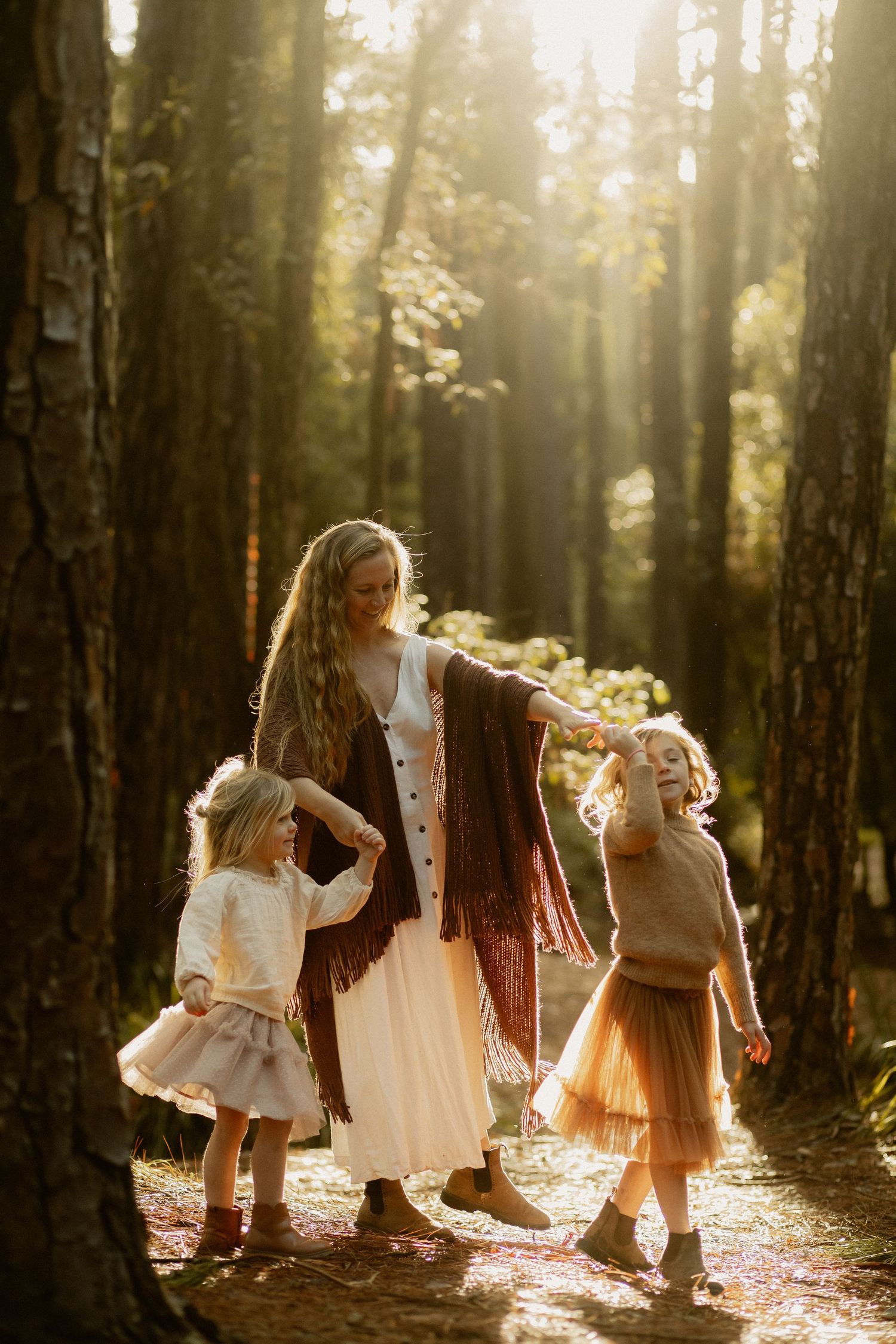 Children in flowing vintage dresses dancing in rays of golden sunlight filtering through a misty forest.
