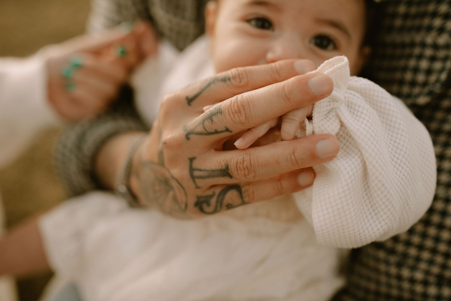 Close up view of tattooed hands holding a baby wrapped in white cloth.
