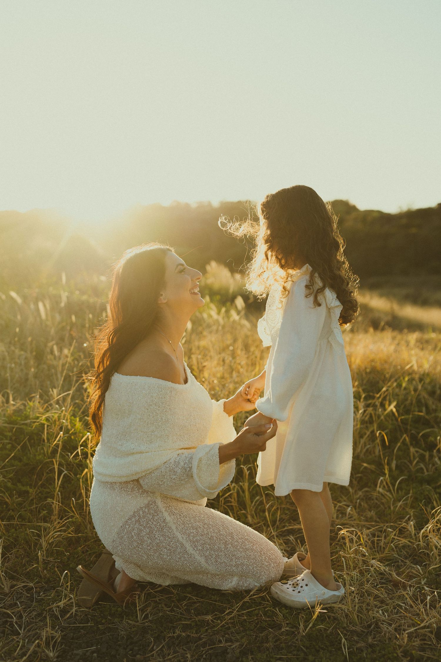 A tender moment captured between two people in white outfits against a warm sunset backdrop.