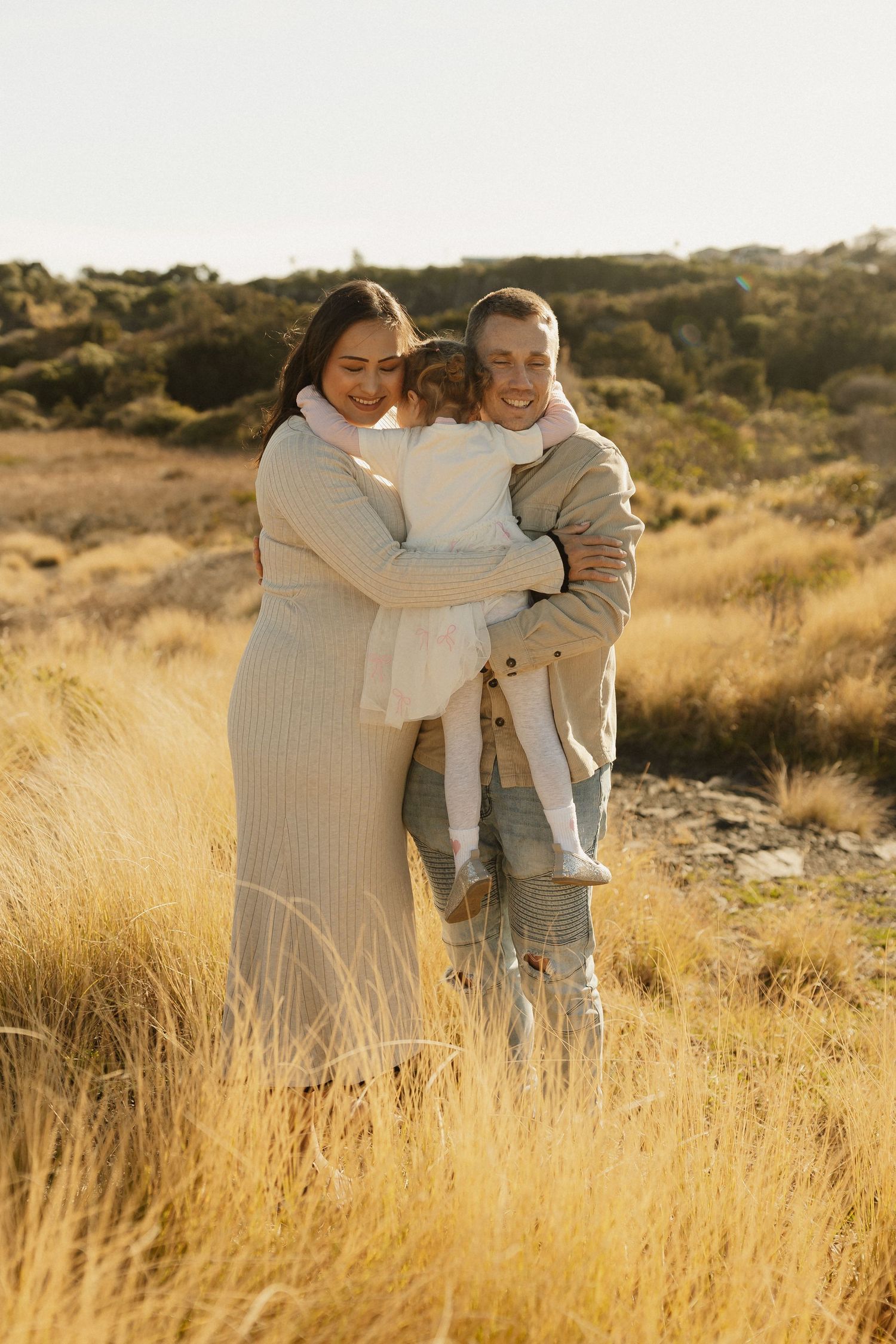 A loving family poses together in golden sunlit grass during a warm outdoor photoshoot.