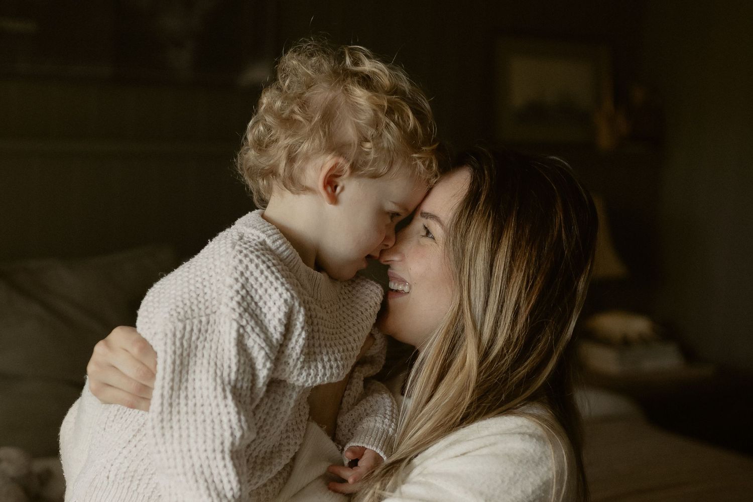Parent and child embracing in tender moment with soft natural lighting against wooden wall background.