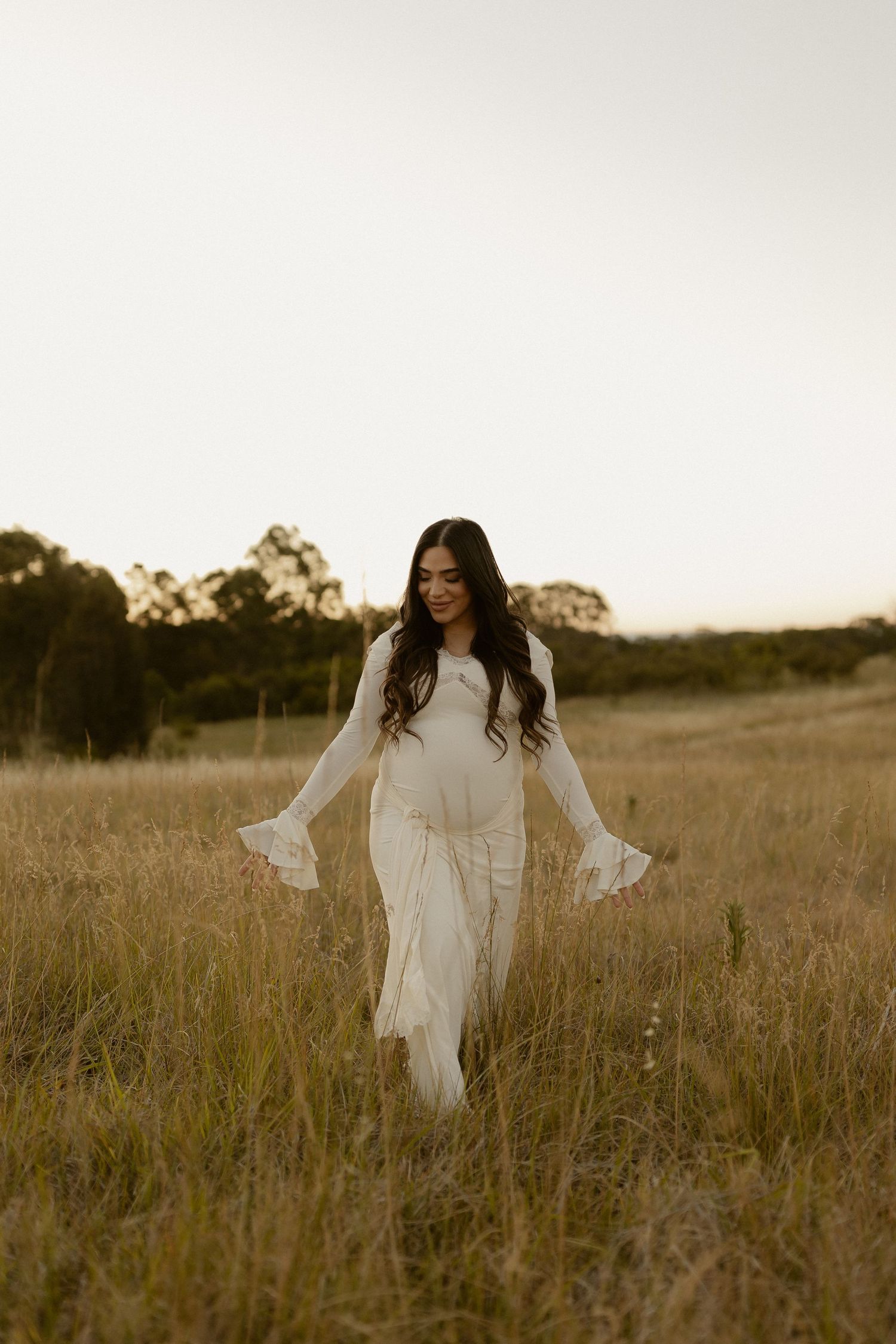 A person in a flowing white dress twirls joyfully in a sun-drenched meadow during golden hour.