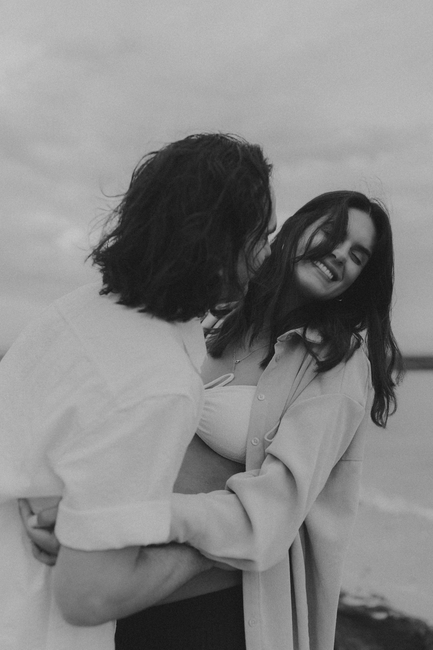 A joyful couple embraces in a candid black and white moment at the beach.