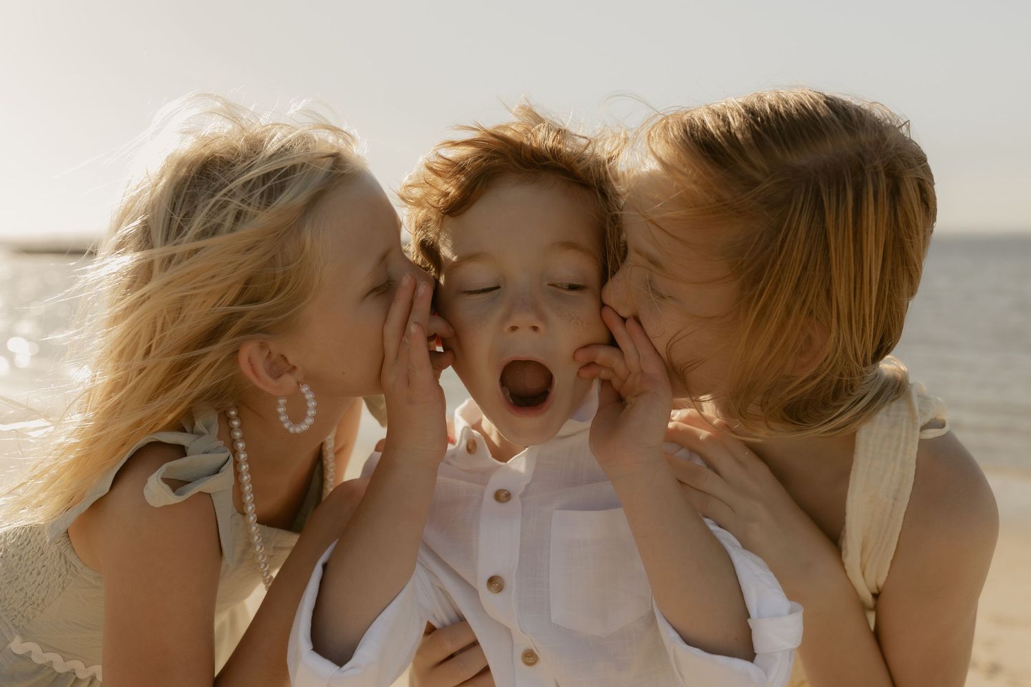 A candid moment of three people sharing secrets and expressions of surprise at sunset by the ocean.