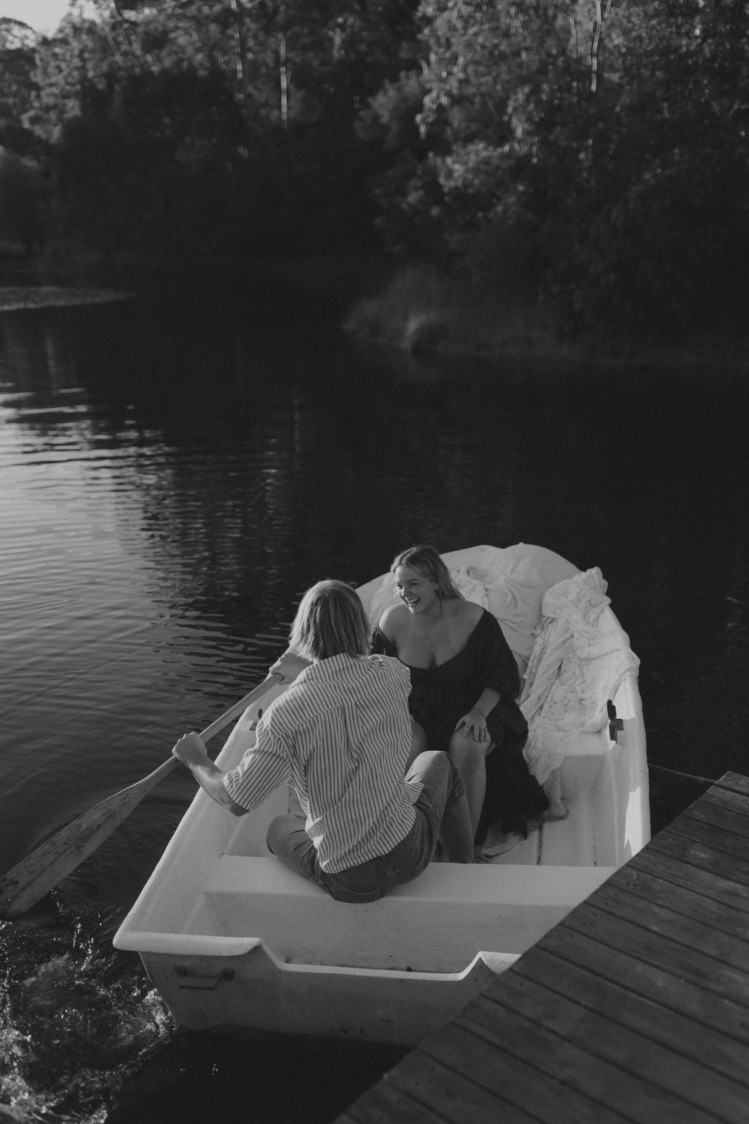 Couple relaxing on a white mattress on wooden dock by serene lake.