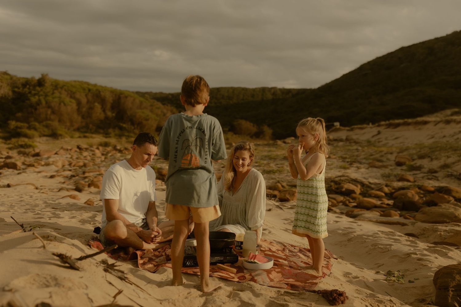 A family enjoys a relaxing picnic together on a rocky beach during sunset.