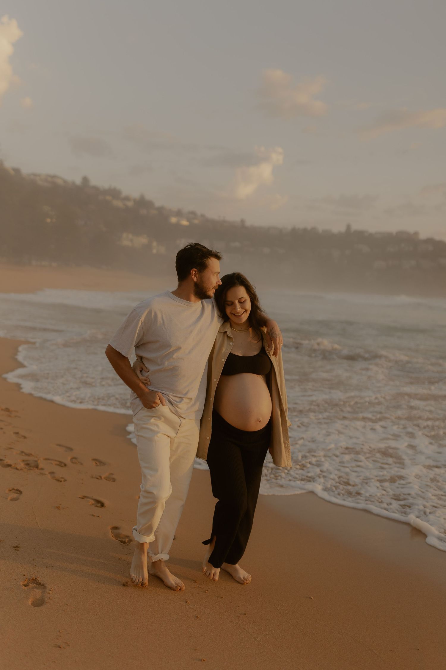 A couple shares joyful moments together during sunset on a sandy beach with waves crashing in the background.