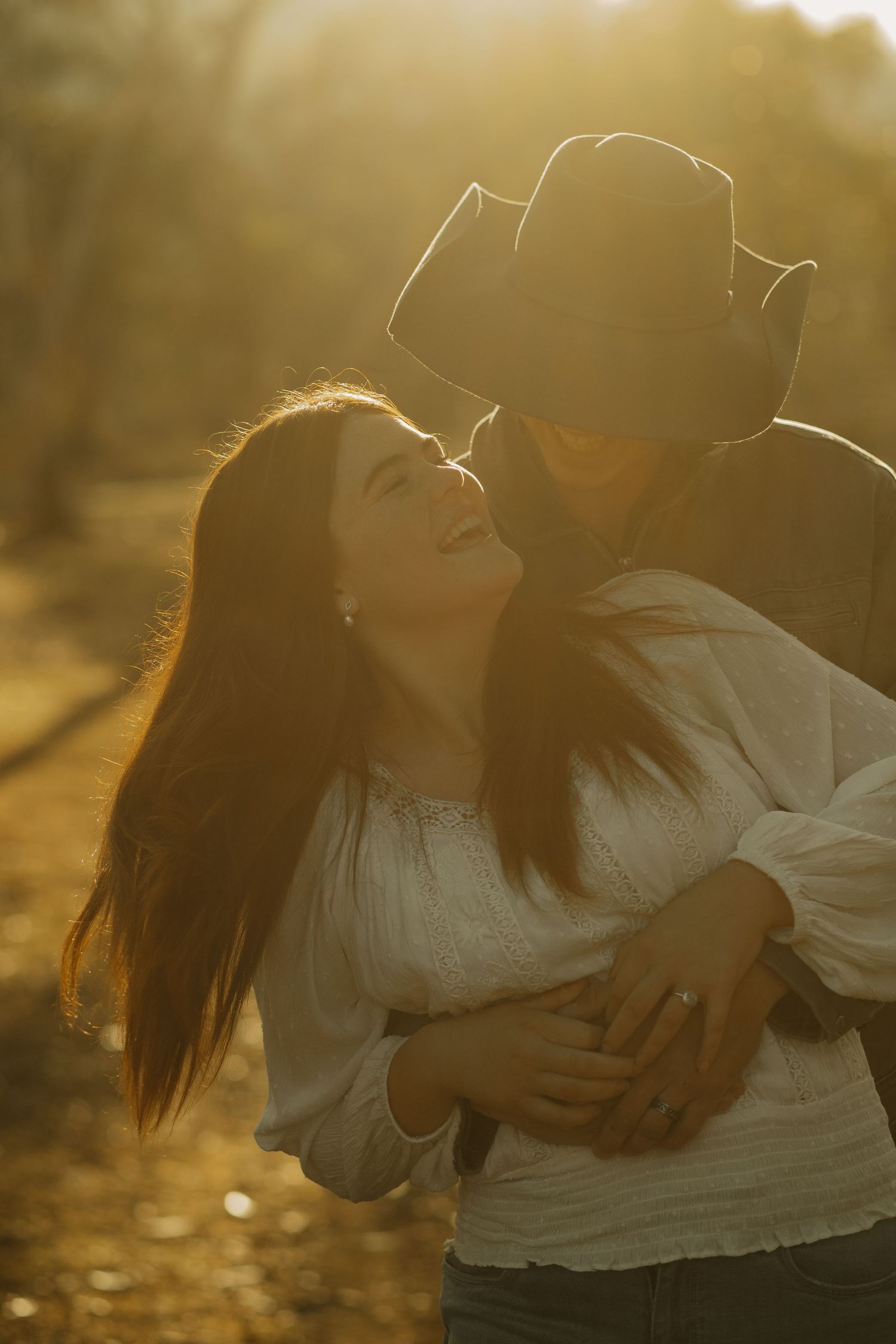A romantic sunset portrait showing tender embrace among tall grass and trees.