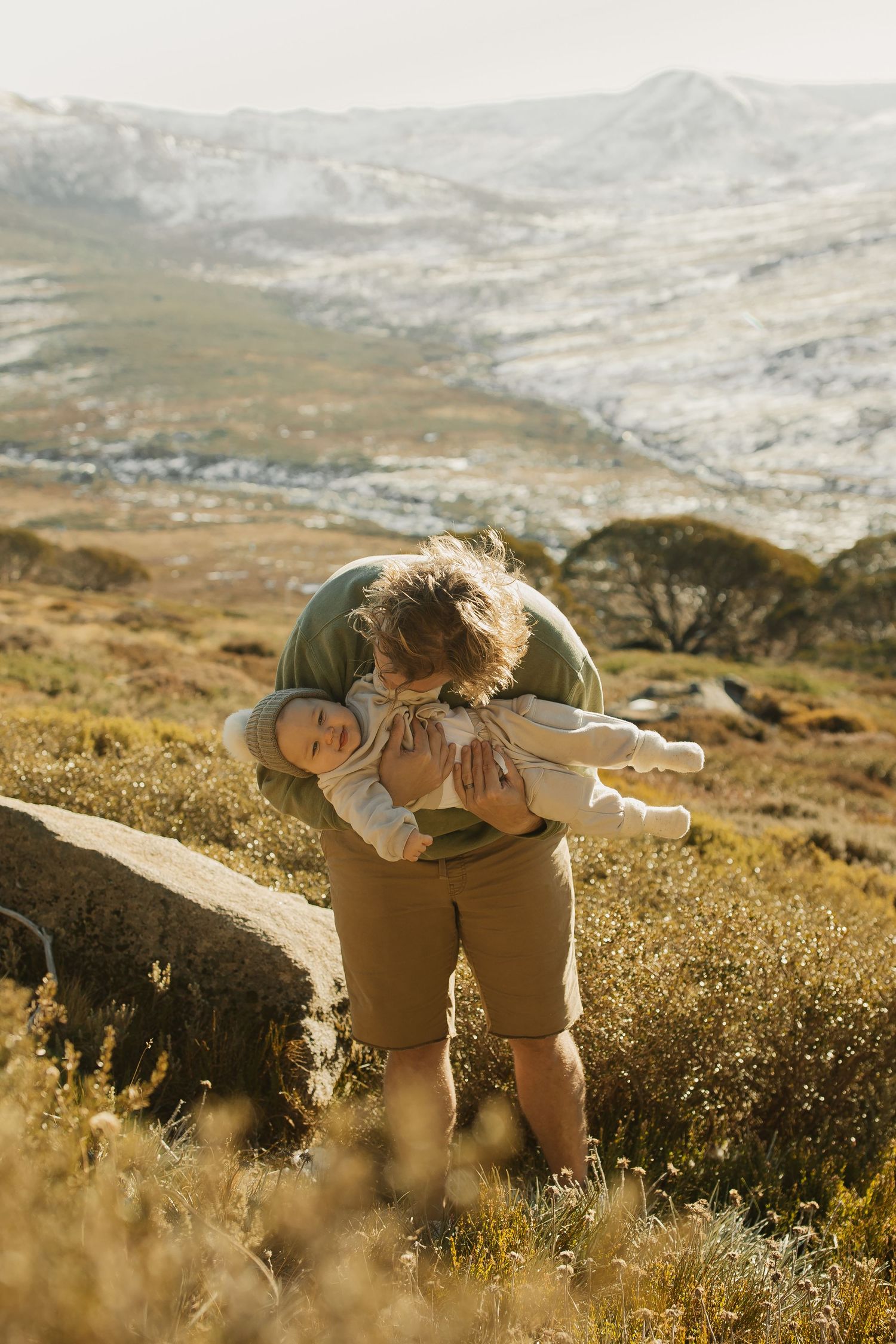 A playful moment captured outdoors with a small child being lifted up against a mountainous landscape.